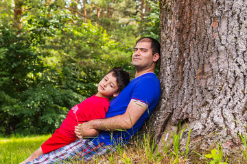 father and son resting under a tree in the summer