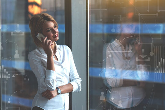 Portrait of a young businesswoman talking on cellphone while standing by office window with infographic design elements, female entrepreneur having mobile phone conversation with copy space for text
