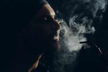 Man smoking a pipe on dark background. Back lit profile portrait.