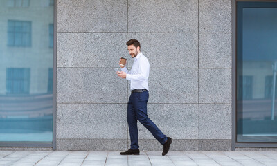 Confident CEO with coffee and mobile phone walking near office building in city center