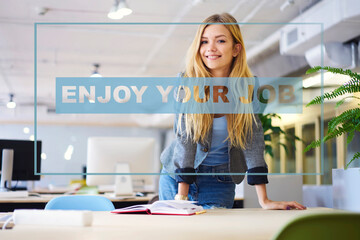 Half length portrait of positive female standing at table with book and working teacher in college.Cheerful young creative tutor with blonde hair in stylish classroom smiling at camera during break