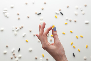 Female hand with tablet between the fingers on a white background. Randomly scattered tablets.