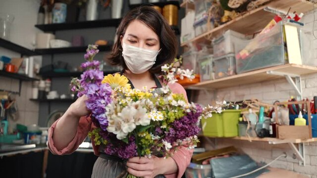 woman in fasial protective mask fixing flowers. Young female florist composing a bouquet of chamomile in a flower shop or workshop. concept virus prevention, covid19 epidemic