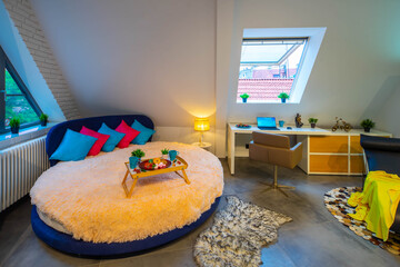 Loft interior of bedroom in modern apartment. Tray on the round bed. Roof window. Chair and table...