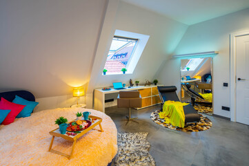 Loft interior of bedroom in modern apartment. Tray on the round bed. Roof window. Place to work. Lounge chair. Huge mirror.