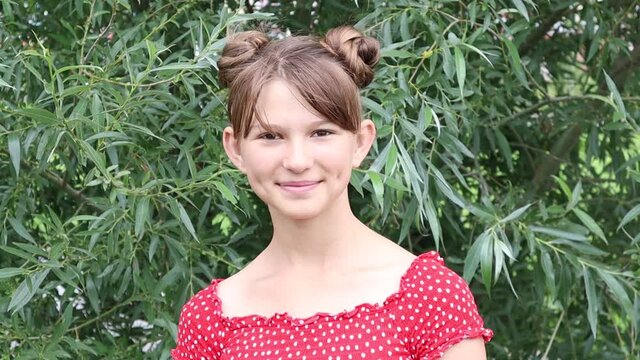 Portrait of smiling looking girl with dimples on red dress. Play with the camera. Rotates her head.