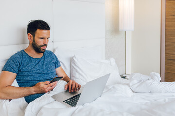 Young man working on laptop in bed