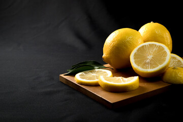 Fresh yellow lemon lime fruit with slices and fresh lemon juice on wood cutting board on black...