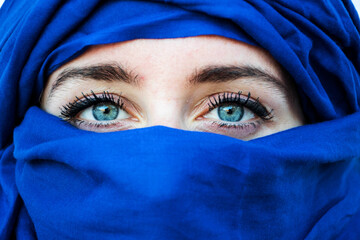 young woman with bright blue headscarf and blue eyes. Nomadic desert outfit. Morocco, merzouga....