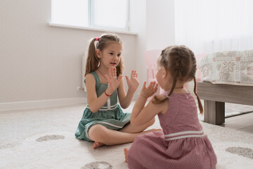 Cute little sisters playing together sitting on the carpet in identical dresses different colors in a room with lots of light