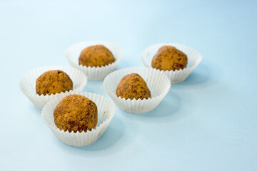 Sweet energy candy balls in white paper tins on a blue background. The concept of raw food desserts from dates, nuts, coconut, seeds, sugar and gluten free.