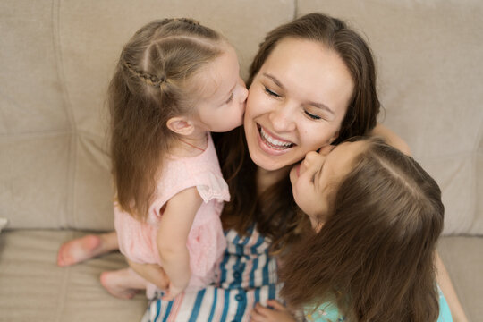 Lovely little daughters kissing sweet their sunny mother on checks. Happy family concept