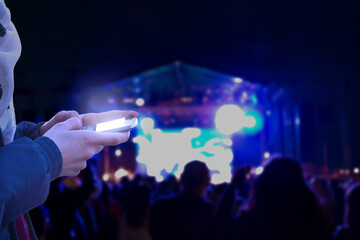 Woman using modern smartphone at night with blurred concert lights in background.