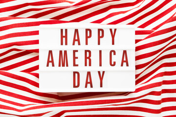 HAPPY AMERICA DAY written in light box on red background. Top view, copy space. Independence day concept