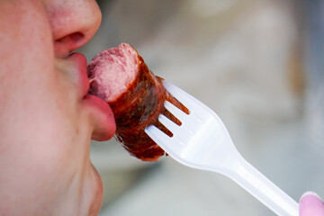 The girl bites off a grilled sausage on a fork. Girl eating a sausage close up