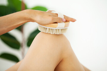 Woman's arm holding dry brush to top of her leg, cellulite treatment and dry brushing.