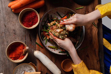 Asian women wearing Korean traditional costumes (hanbok) are mixing fresh stir-fry and kimchi...