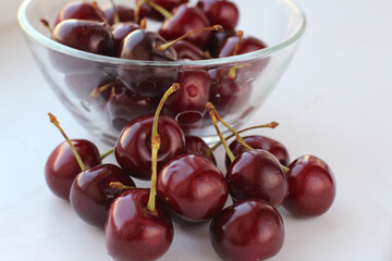 Fresh cherry berries with drops of water in a glass plate on a white table. Close-up macro shot