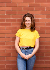 portrait of a young woman wearing yellow shirt against brick wall