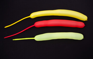 Three balls of yellow, lemon and red are on a black surface. The balls are long with the remaining unsneed ends