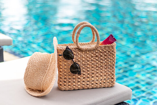 Weaving bag and hat with sunglasses and sunscreen lotion next to a swimming pool, summer travel concept
