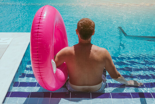 Happy man is sleeping and relaxing on big pink inflatable ring at swimming pool on summer day.