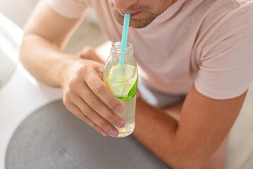 Man drinks lemonade through a straw from glass bottle.