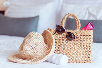 Summer trip preparation with weaving hat, bag, sunglasses and sunscreen lotion on a white bed