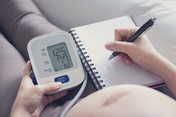 Pregnant woman measuring blood pressure at home, health check of expecting mom
