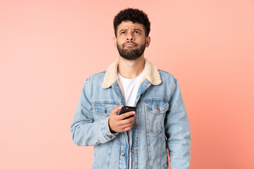 Young Moroccan man using mobile phone isolated on pink background and looking up