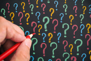 Man drawing colorful question marks with a pencil on black paper