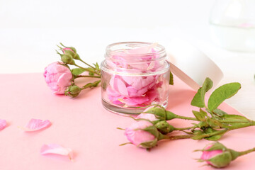 A jar with rose petals, rose blossoms and scattered petals on a pastel background, close-up, side view - the concept of skin care
