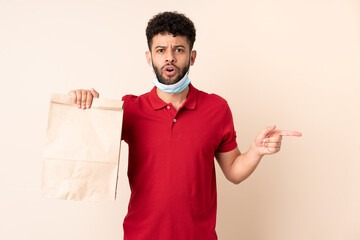 Young man holding a takeaway food bag ___ surprised and pointing side