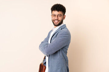 Young business Moroccan man isolated on beige background with arms crossed and happy