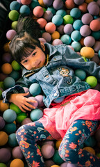 Fototapeta na wymiar Little Asian girl in a ball pit smiling at the camera, having fun at the children play center