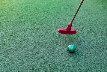 Closeup of toy golf ball and putter on the green grass