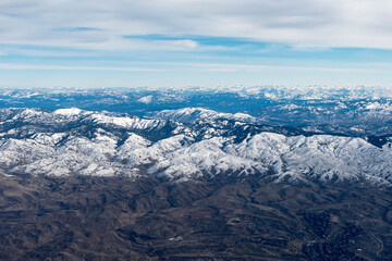 Aerial View of Idaho mountains from the sky while inside an airplane. View of brown mountains and trees covered with snow
