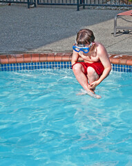 This 7 year old Caucasian boy is wearing a swimming mask, while doing a cannon ball, mid air into a pool of water.  Great summer childhood fun.