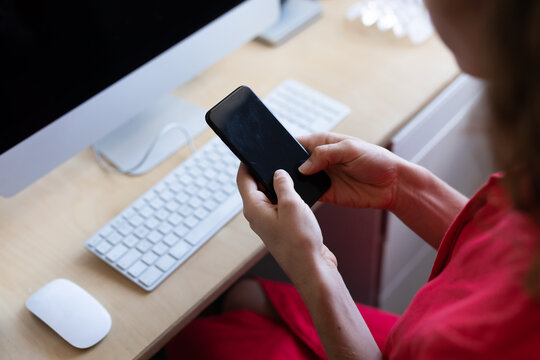 Caucasian woman sitting by her desk and using her smartphone