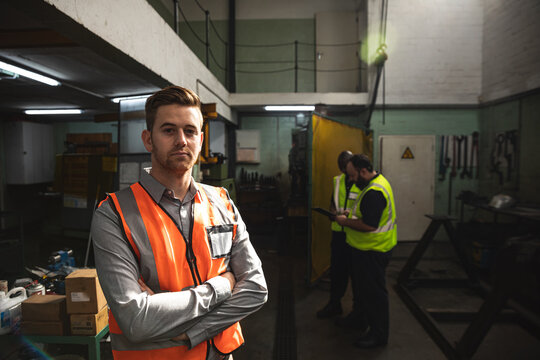 Male factory worker wearing a Hi-vis vest standing with his arms crossed at the factory