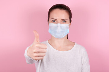 Portrait of a brunette girl in a medical mask, thumb up gesture.