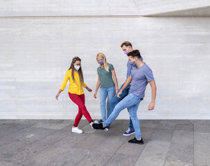 Fototapeta premium Group of young friends meet and greet each other with their feet - Multiracial people wearing face masks - Concept of social distance and health care
