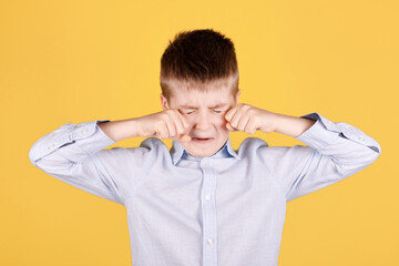 Portrait of a brunette boy crying with hands. Isolated on yellow background.