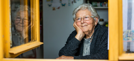 Portrait of lovely senior woman or grandmother watching out from the window and smiling