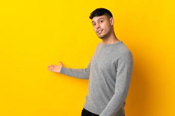 Young Colombian man isolated on yellow background extending hands to the side for inviting to come