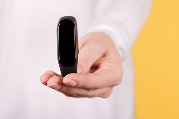 Black smart fintess band in hand on yellow background. Close up photo.