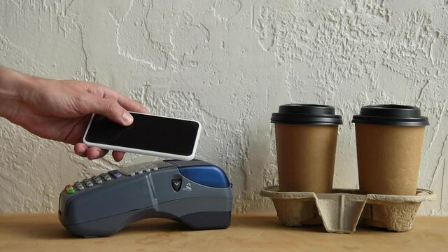 cropped view of man using smartphone and payment terminal near paper cups 