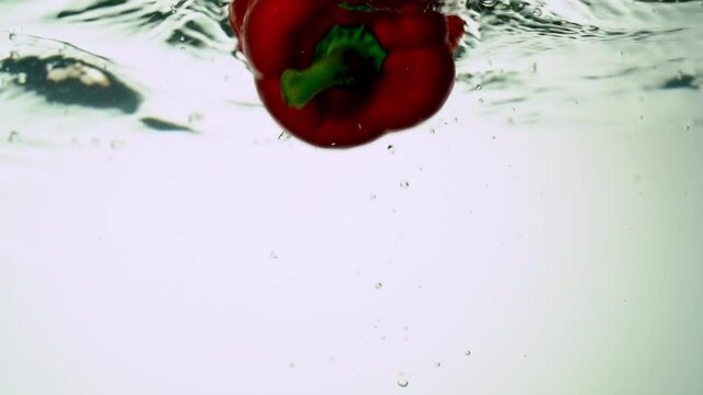 Ecological pure red sweet bell pepper is immersed in water, creating bubbles. On white background.