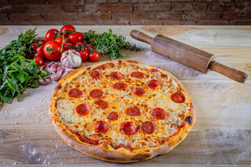 Pepperoni pizza and cooking ingredients: tomatoes, basil, garlic on wood table background
