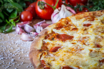 Pepperoni pizza and cooking ingredients: tomatoes, basil, garlic on wood table background